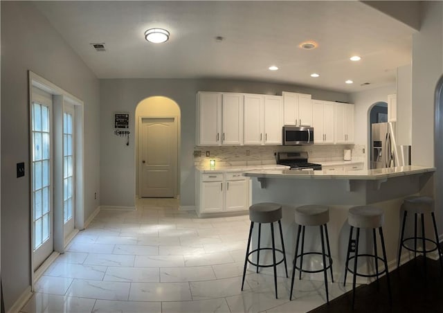 kitchen featuring kitchen peninsula, a kitchen breakfast bar, backsplash, stainless steel appliances, and white cabinetry