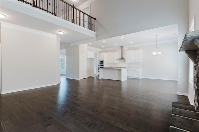 unfurnished living room with baseboards, a stone fireplace, crown molding, dark wood-type flooring, and a high ceiling