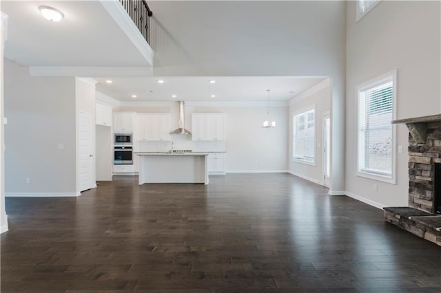 unfurnished living room with a towering ceiling, dark wood-type flooring, a fireplace, crown molding, and baseboards