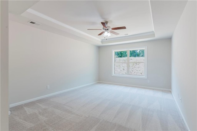 unfurnished room featuring a tray ceiling, baseboards, ceiling fan, visible vents, and light colored carpet