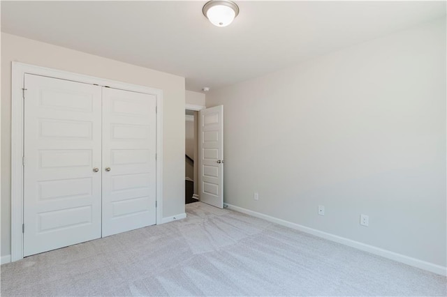 unfurnished bedroom with baseboards, light carpet, and a closet