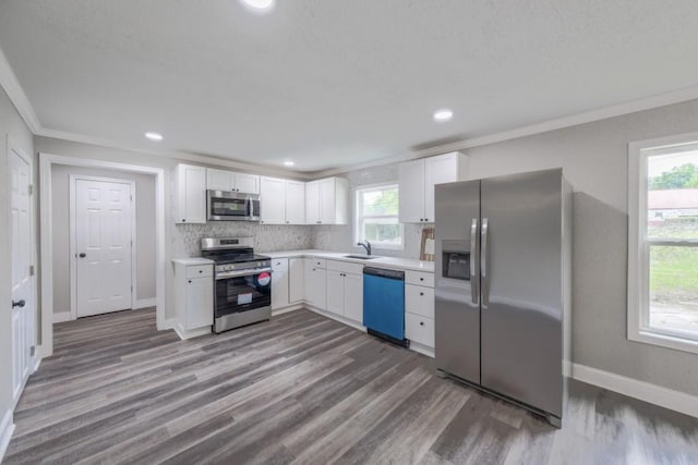 kitchen with stainless steel appliances, a sink, ornamental molding, light countertops, and white cabinets