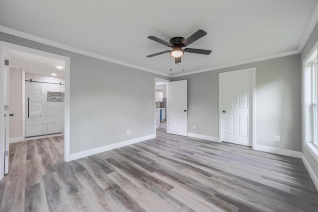 unfurnished bedroom featuring crown molding, wood finished floors, baseboards, ensuite bath, and a ceiling fan