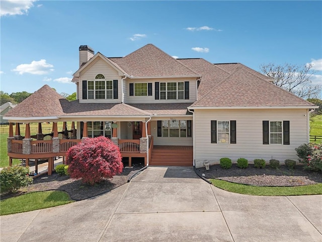 view of front of home featuring concrete driveway, a porch, a shingled roof, and a chimney