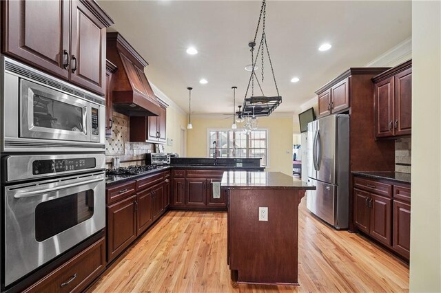 kitchen featuring a center island, crown molding, backsplash, appliances with stainless steel finishes, and light wood finished floors