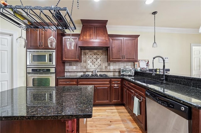 kitchen with ornamental molding, premium range hood, decorative light fixtures, stainless steel appliances, and a sink