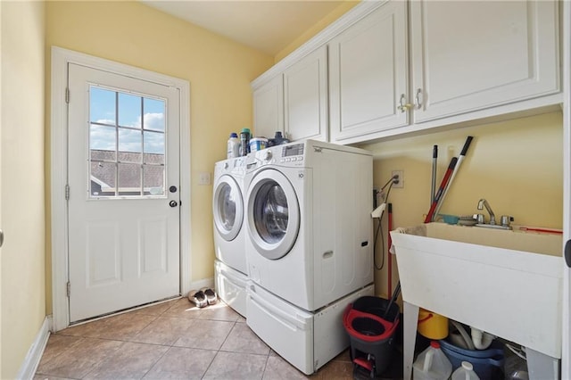 washroom featuring light tile patterned floors, baseboards, a sink, cabinet space, and washing machine and dryer