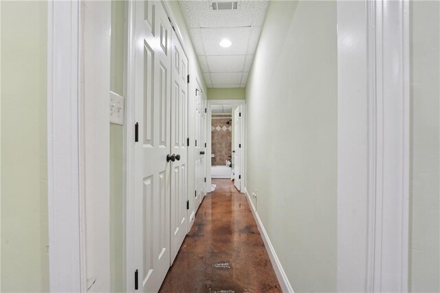hall featuring finished concrete floors, a drop ceiling, visible vents, recessed lighting, and baseboards