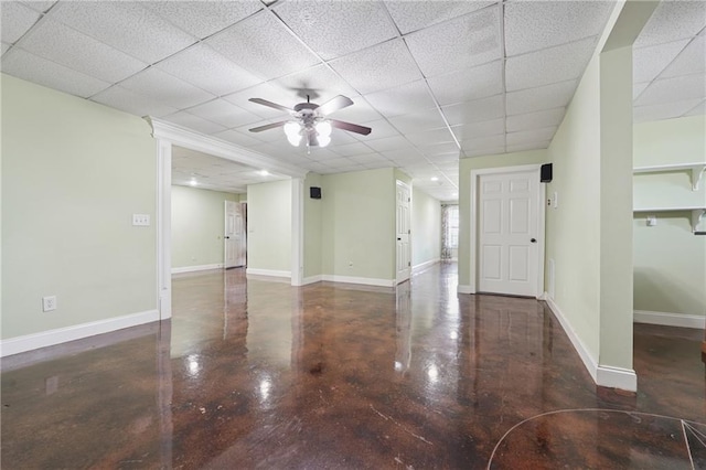 unfurnished living room featuring a drop ceiling, concrete flooring, baseboards, and a ceiling fan