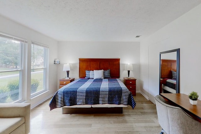 bedroom with light wood-style floors, multiple windows, visible vents, and a textured ceiling