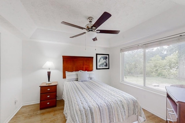 bedroom featuring light wood-style floors, baseboards, a raised ceiling, and a textured ceiling