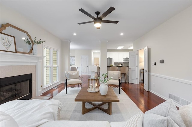 living area featuring a tile fireplace, recessed lighting, dark wood-type flooring, visible vents, and baseboards