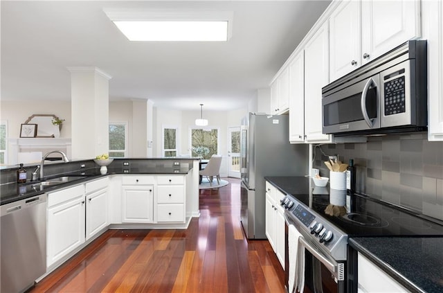 kitchen featuring dark countertops, dark wood-style floors, a sink, stainless steel appliances, and backsplash