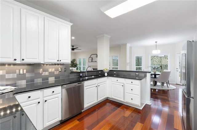 kitchen with stainless steel appliances, dark wood-type flooring, white cabinets, a sink, and a peninsula