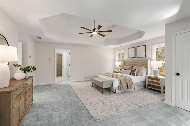 bedroom with ceiling fan, light colored carpet, visible vents, baseboards, and a raised ceiling