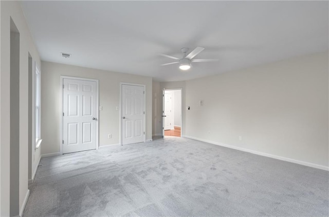 unfurnished bedroom with ceiling fan, carpet flooring, visible vents, baseboards, and multiple closets