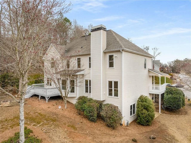 view of side of property with a deck, roof with shingles, a chimney, and a balcony