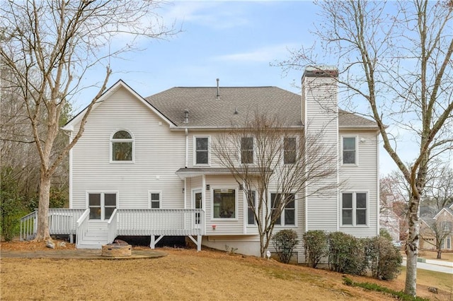 rear view of property featuring roof with shingles, a lawn, a chimney, and a wooden deck