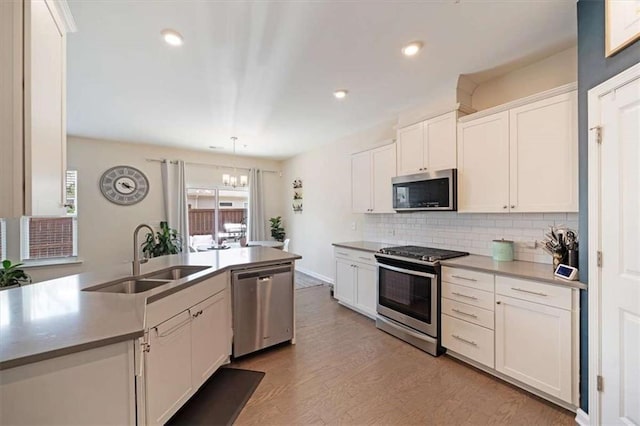 kitchen with sink, pendant lighting, stainless steel appliances, decorative backsplash, and white cabinets