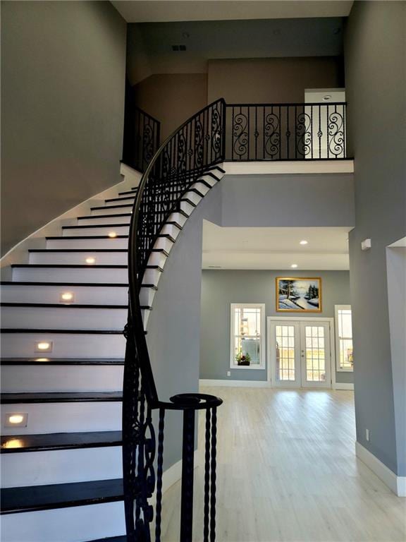 stairs featuring a wealth of natural light, french doors, hardwood / wood-style floors, and a towering ceiling