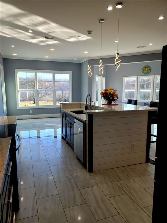 kitchen featuring stove, sink, pendant lighting, light tile patterned floors, and an island with sink