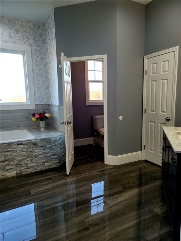 bathroom with a relaxing tiled tub, vanity, tile patterned flooring, and toilet