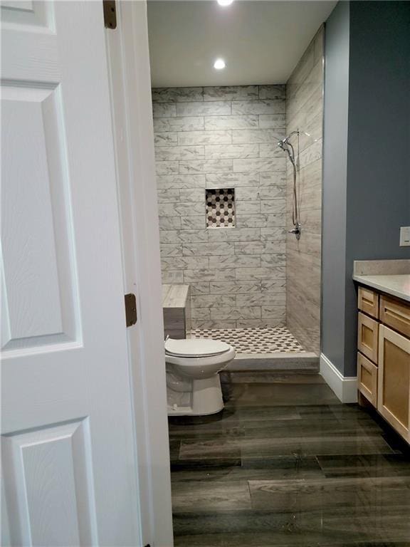 bathroom with hardwood / wood-style flooring, toilet, vanity, and a tile shower