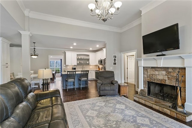 living area with a stone fireplace, ornamental molding, dark wood-type flooring, and an inviting chandelier