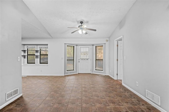 spare room featuring vaulted ceiling, a healthy amount of sunlight, a textured ceiling, and ceiling fan