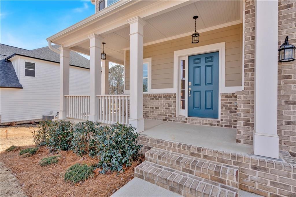 doorway to property with cooling unit, brick siding, and covered porch