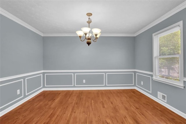 empty room featuring crown molding, wood-type flooring, and an inviting chandelier