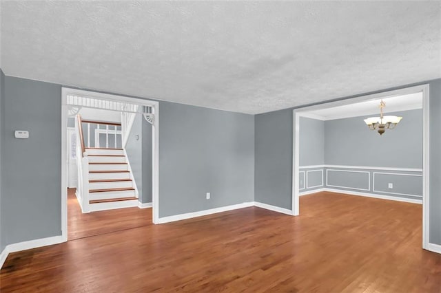 unfurnished living room with wood-type flooring, a textured ceiling, and a notable chandelier