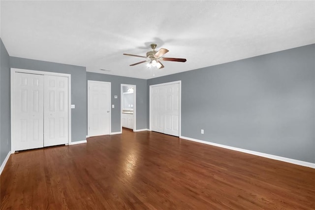 unfurnished bedroom with multiple closets, ceiling fan, and dark hardwood / wood-style flooring