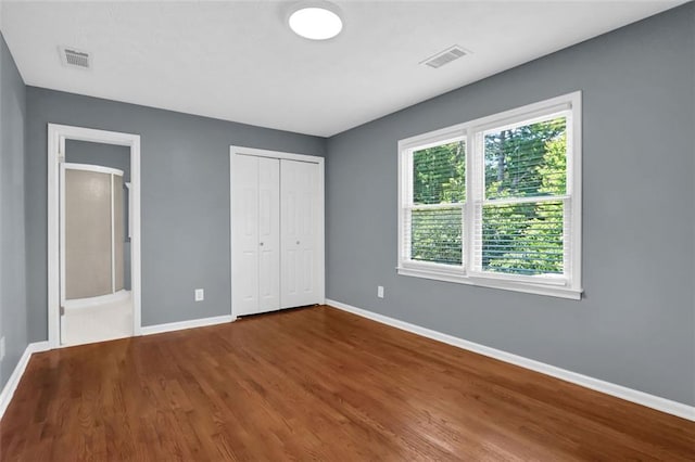 unfurnished bedroom with a closet, hardwood / wood-style flooring, and multiple windows