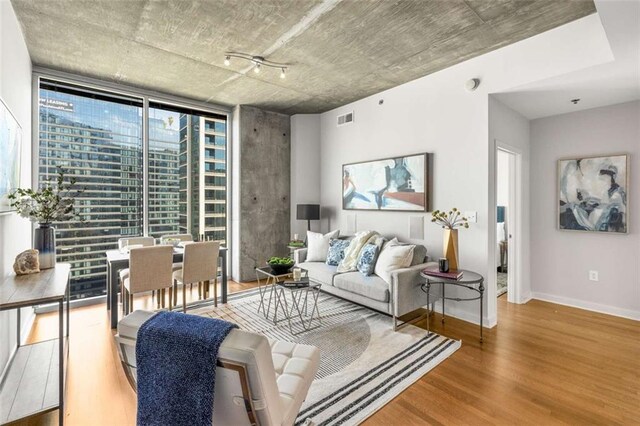 living area with a wall of windows, visible vents, baseboards, and wood finished floors