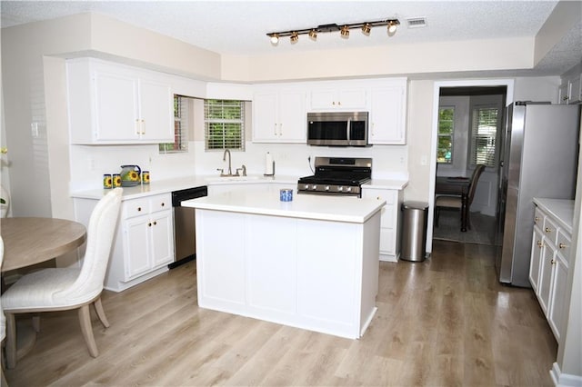 9130 Charlton Pl, Douglasville, GA 30135 - kitchen featuring appliances with stainless steel finishes, light countertops, light wood-type flooring, white cabinetry, and a kitchen island
