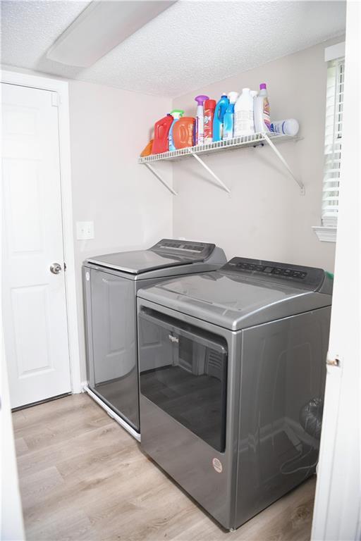 9130 Charlton Pl, Douglasville, GA 30135 - laundry area with washer and clothes dryer, light wood-style floors, and a textured ceiling