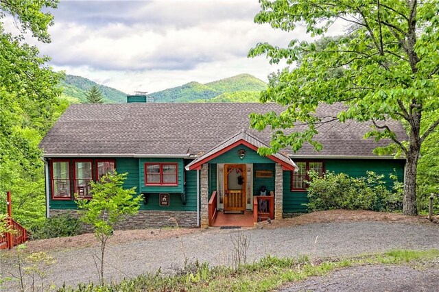 view of front of property featuring a mountain view, a chimney, a shingled roof, and stone siding