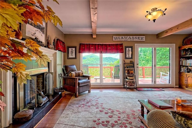 living area with a tile fireplace, beamed ceiling, and wood finished floors