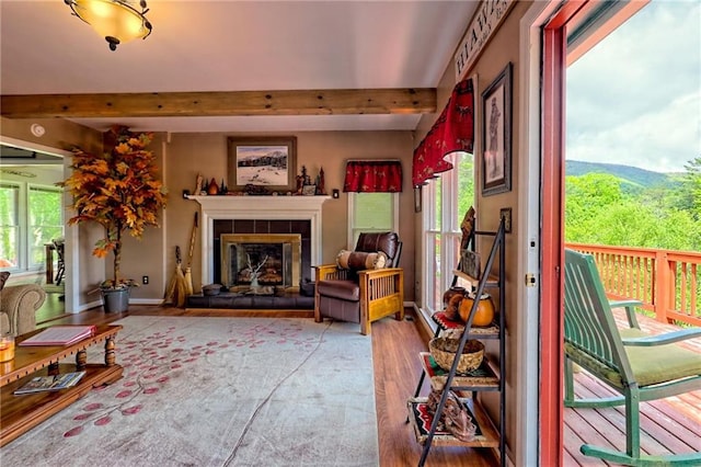 living area with beamed ceiling, wood finished floors, and a tiled fireplace