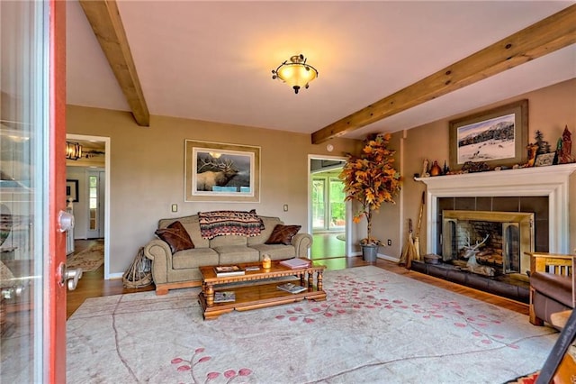 living area with wood finished floors, baseboards, beamed ceiling, and a tiled fireplace