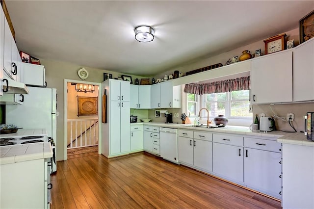 kitchen with dishwasher, a sink, tile counters, wood finished floors, and white cabinets