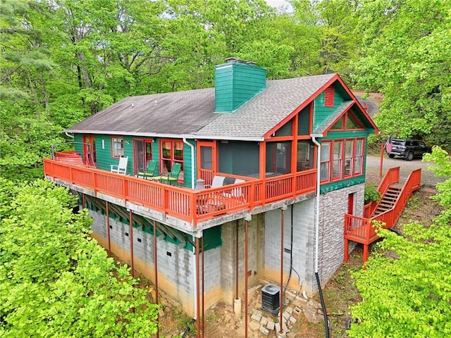 rear view of property featuring a shingled roof, a chimney, a wooden deck, central AC unit, and stairway