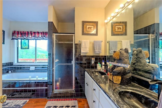 bathroom featuring a shower stall, double vanity, a garden tub, wood finished floors, and tile walls