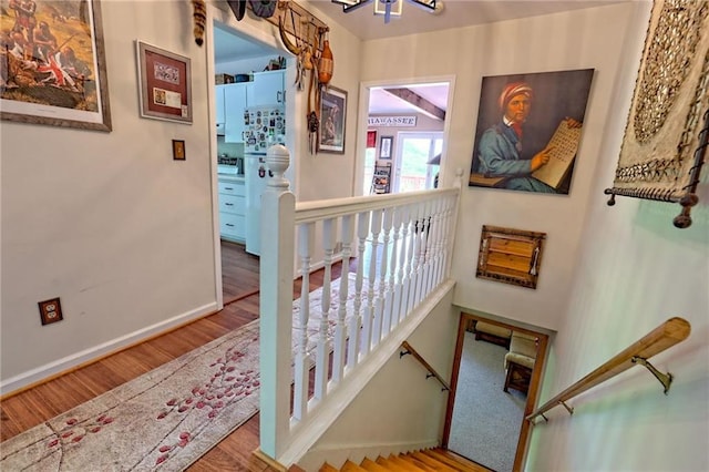 stairway with wood finished floors, baseboards, and a chandelier