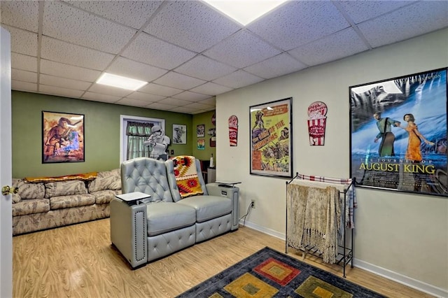 living area with wood finished floors, a paneled ceiling, and baseboards