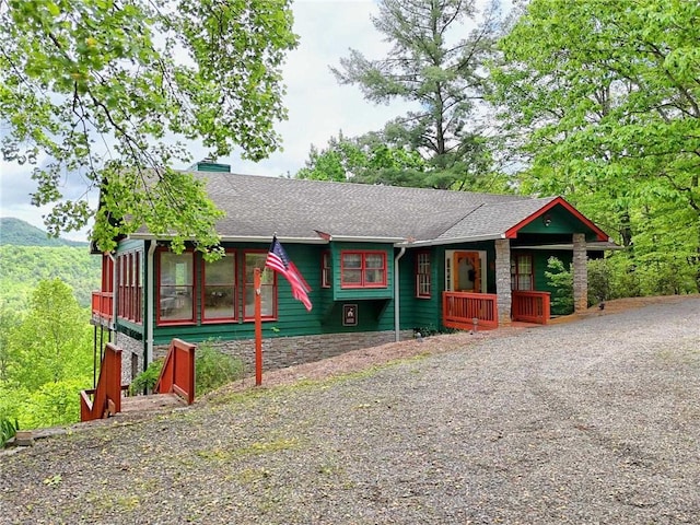 view of front facade with stone siding, a shingled roof, and a sunroom