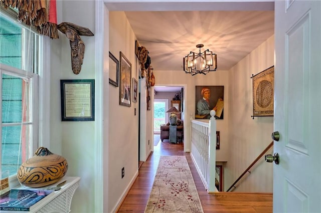 hallway with a chandelier, wood finished floors, an upstairs landing, and baseboards
