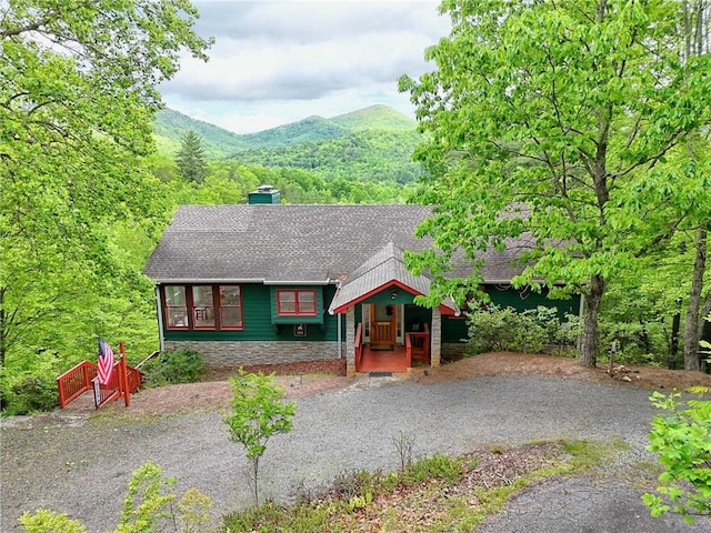 view of front of house with roof with shingles, stone siding, a mountain view, a chimney, and a porch