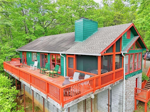 back of house featuring a shingled roof, a wooden deck, a chimney, and a sunroom